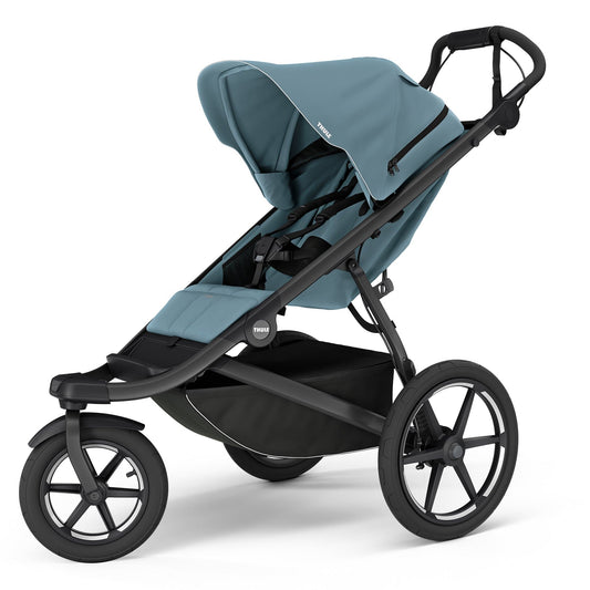Mid blue single jogging stroller by Thule with black frame, large air-filled wheels, and magnetic buckle harness, side view
