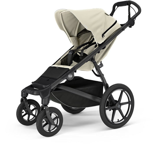 Soft beige all-terrain stroller by Thule with black frame, large wheels, and extended canopy, side view