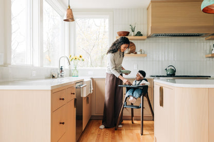 Woman feeding a baby in a high chair in a modern kitchen