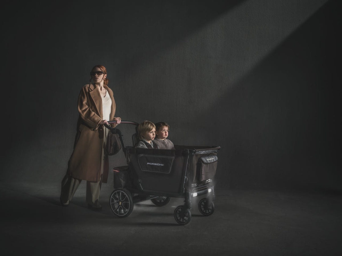 WonderFold Porsche edition stroller with two children inside being pushed by a woman